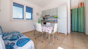 A compact kitchen with white cabinets, a dining table with chairs, and a window with blinds. - Holiday Home "Sottotorre 2" close to the Sea with Private Garden & A/C (Calasetta)