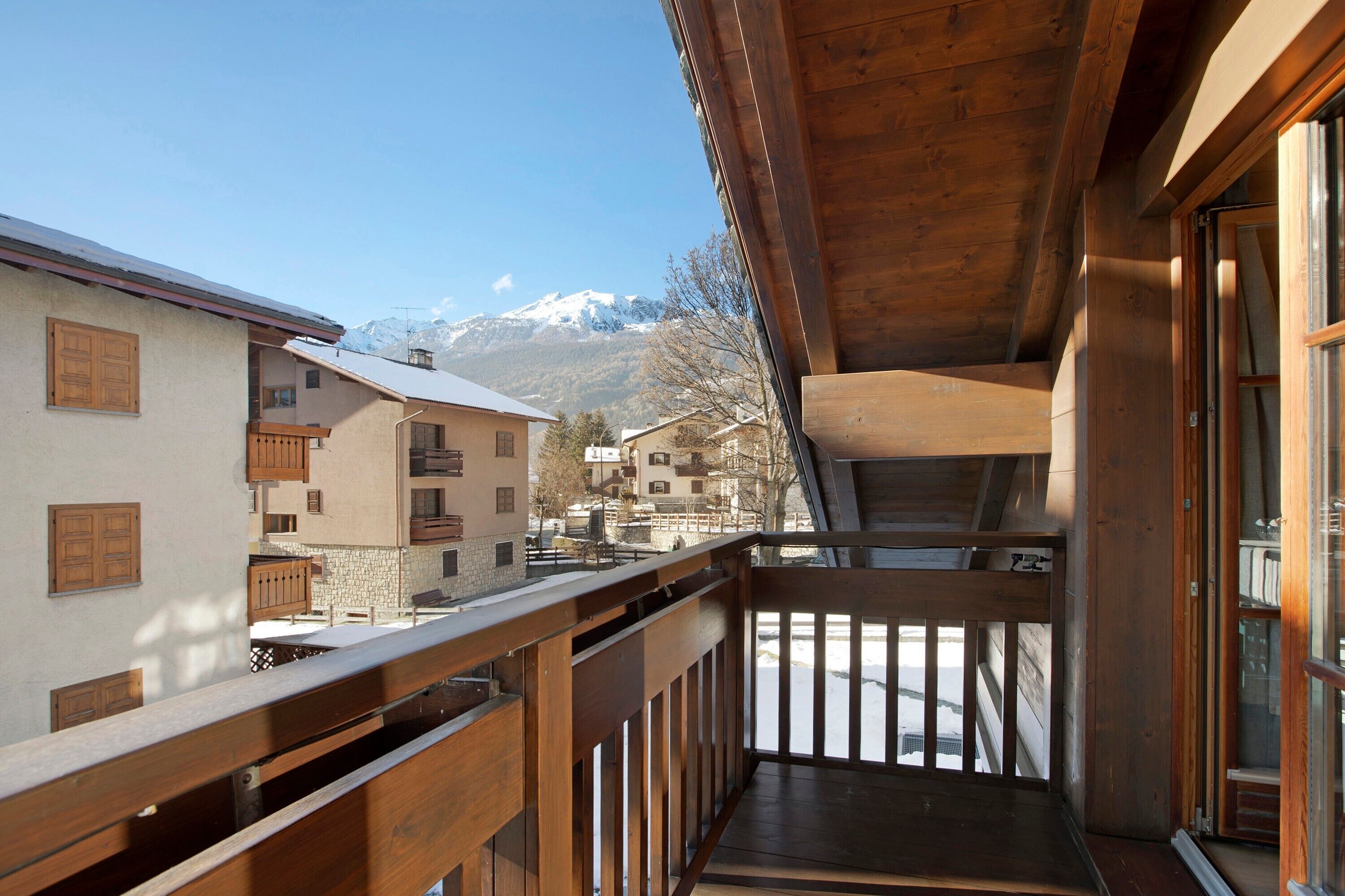 Un balcón de madera con vistas a montañas nevadas y edificios cercanos.