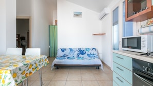 A compact room with a bed, a dining table, a kitchenette, and a small window.
