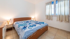 A bedroom with a bed, bedside tables, a nightstand, a window with curtains, and a wall-mounted lamp.