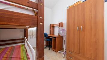 A bedroom with a bunk bed, a desk with a chair, a wardrobe, and a standing fan.
