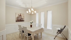 Ein Esszimmer mit einem runden Tisch, weißen Stühlen, einer Kristallleuchter und einer Blumenvase.