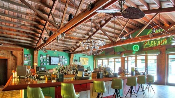 A bar with a wooden ceiling and green chairs.