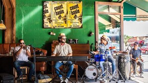 A band performing in a room with green walls, a piano, drums, and a keyboard.