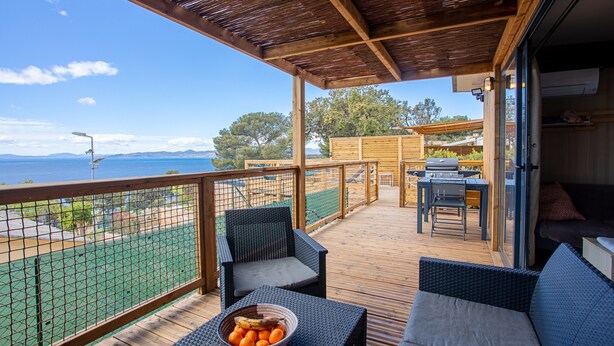 Eine überdachte Terrasse mit Gartenmöbeln, Blick auf das Meer und ein Basketballplatz.