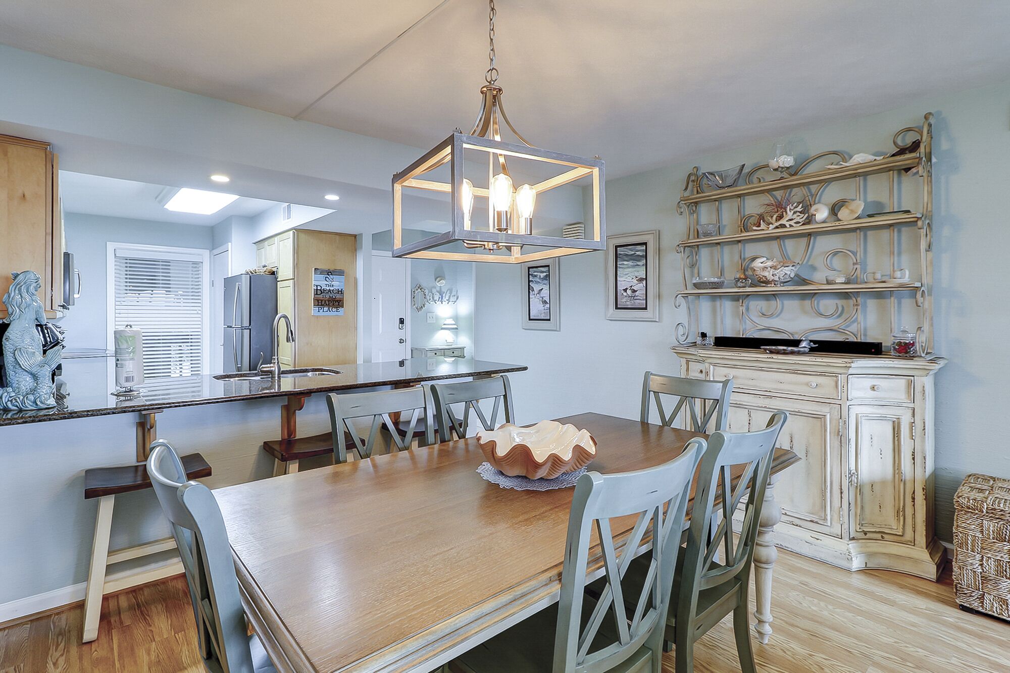 A spacious kitchen with a wooden dining table, chairs, and a hanging light fixture.