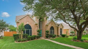 A brick house with a front yard, a large tree, and a wooden fence.