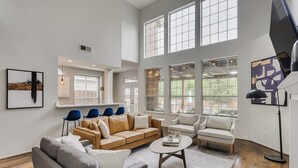 A spacious living room with a large window, a sofa set, a coffee table, and a floor lamp.