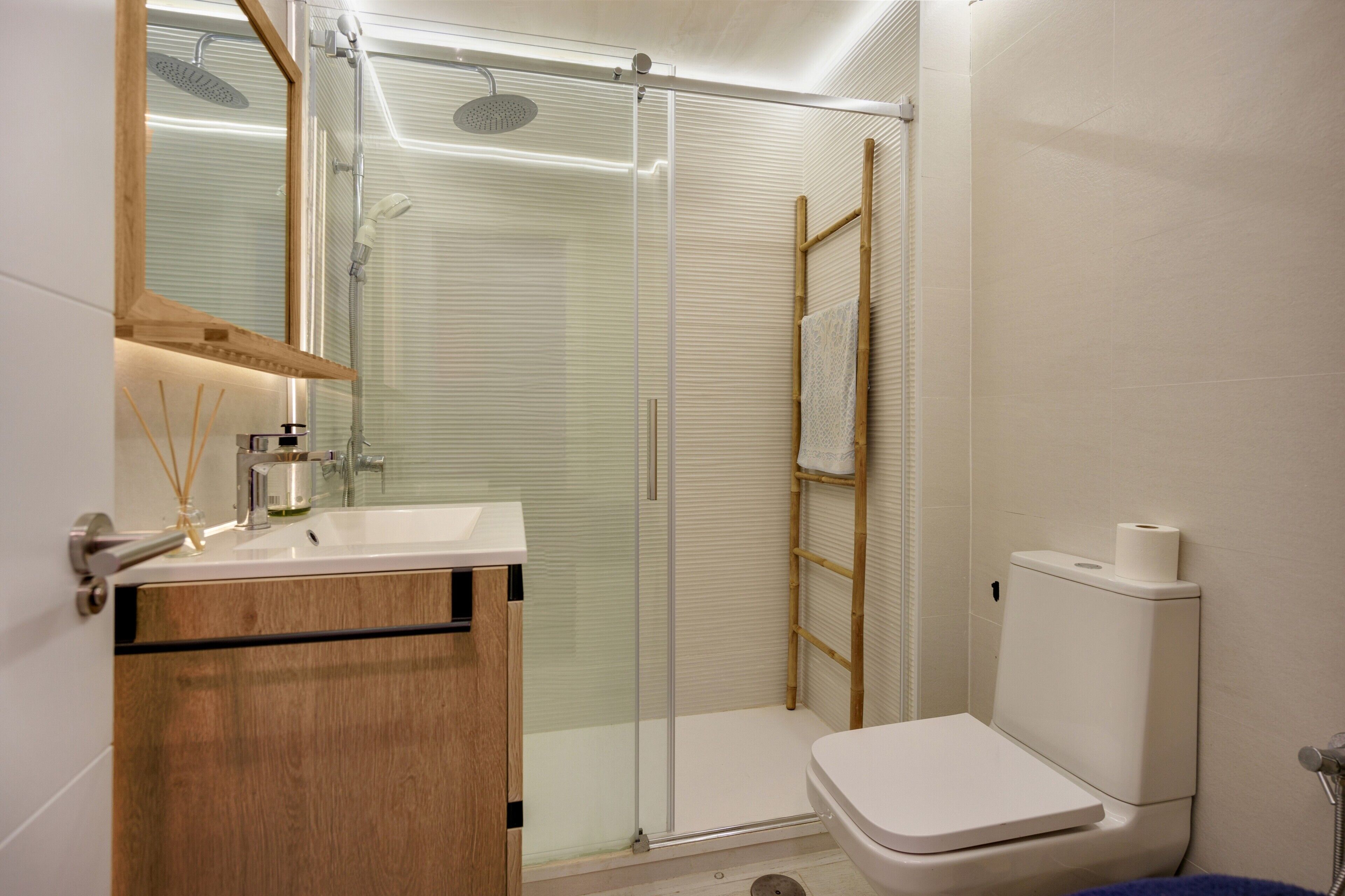 Un baño moderno con ducha acristalada, tocador de madera y un inodoro.