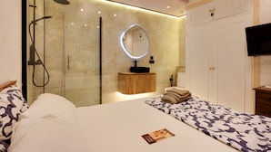 A modern bedroom with a glass-enclosed shower, a round mirror, a wooden vanity, a television, and a neatly made bed. - Apartment “Chipiona, Cruz del Mar 1st Line” with Sea Views, Terrace, Parking & Wi-Fi (Chipiona)