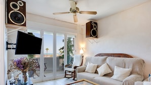 A living room with a sofa, a coffee table, a TV, and speakers. - Apartment “Chipiona, Cruz del Mar 1st Line” with Sea Views, Terrace, Parking & Wi-Fi (Chipiona)