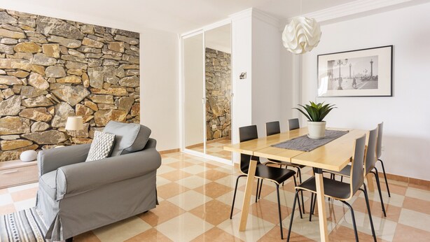 Una sala moderna con una pared de piedra, un sofá, una mesa de comedor con sillas y una planta en maceta.