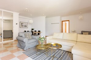 Un salon avec un canapé gris, un canapé blanc, une table basse et un tapis à motifs.