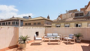Una terraza en la azotea con mobiliario exterior, plantas en macetas y vistas despejadas de los edificios circundantes.