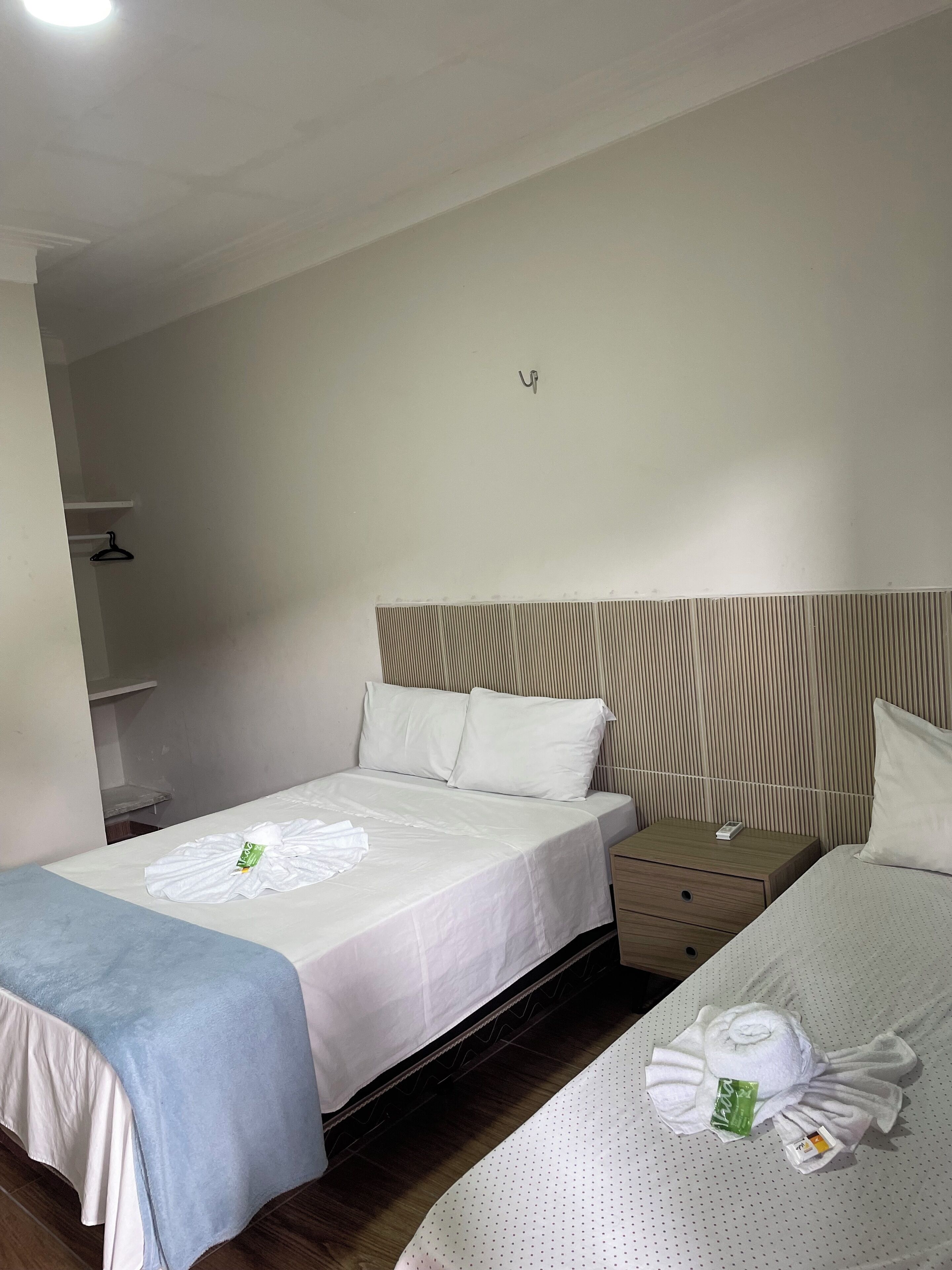 Una habitación de hotel con dos camas, una mesita de noche, un cajón pequeño y una estantería en la pared.