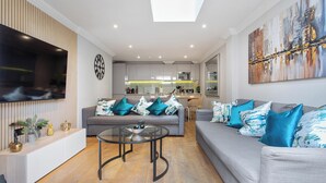 A modern living room with a grey sofa, a glass coffee table, and a flat-screen TV mounted on the wall. - Brand New Development. 5 Star Luxury flat with garden (London,)