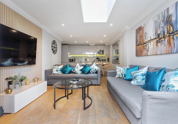 Een moderne woonkamer met een grijze bank, een glazen salontafel en een wandgemonteerde flatscreen-tv.