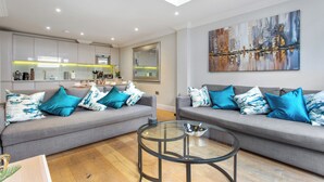 A modern living room with two grey sofas, a glass coffee table, and a cityscape painting on the wall. - Brand New Development. 5 Star Luxury flat with garden (London,)