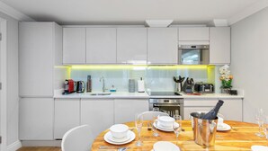 A modern kitchen with white cabinets, a wooden dining table set for four, and a bottle of champagne in a bucket. - Brand New Development. 5 Star Luxury flat with garden (London,)
