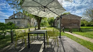 Terrassa exterior amb taula i cadires sota un parasol gran, envoltada de vegetació i edificis històrics.