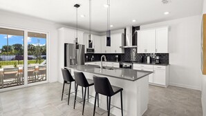 Una cocina moderna con una isla grande, armarios blancos y una puerta corredera de vidrio que da a un patio exterior.