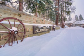 A wooden sign with a large wheel and the text "THE CLAIMJUMPER" in front of a snowy landscape with pine trees.