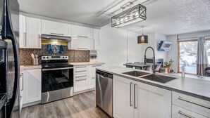 A modern kitchen with white cabinets, stainless steel appliances, and a large island with a sink. - Claimjumper Condo - Hot Tub, Pool, Bus Route, Free Parking (Breckenridge)