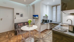 Una cocina moderna con horno empotrado, microondas y lavaplatos. Hay un comedor con una mesa y sillas blancas.