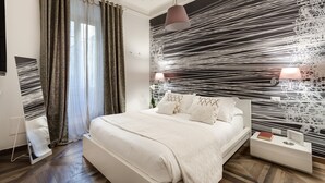 Un dormitorio moderno con una cama grande, una mesita de noche con lámpara y una pared con un diseño blanco y negro llamativo.