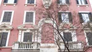 Un edificio de varios pisos con fachada rosa, varios balcones y una entrada central con una gran puerta de madera.