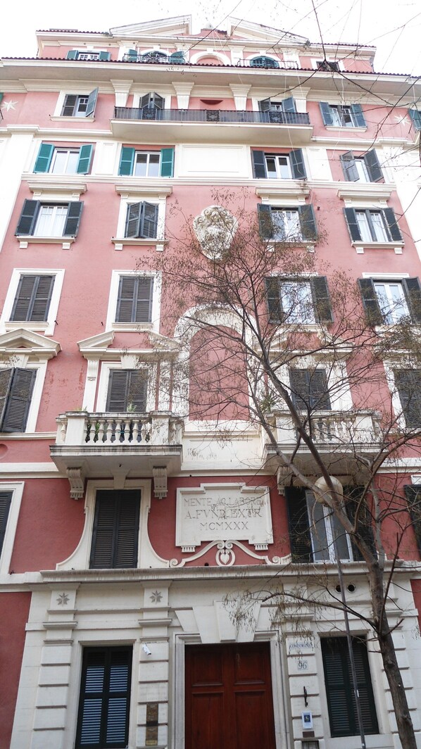 A multi-story building with a pink facade, multiple balconies, and a central entrance with a large wooden door.