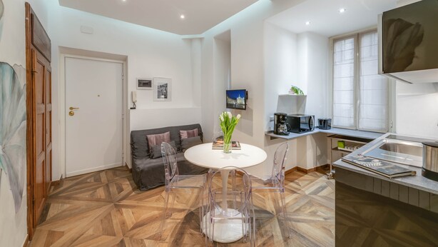 Una cocina moderna con comedor, que incluye una mesa blanca, sillas transparentes y un suelo de madera.
