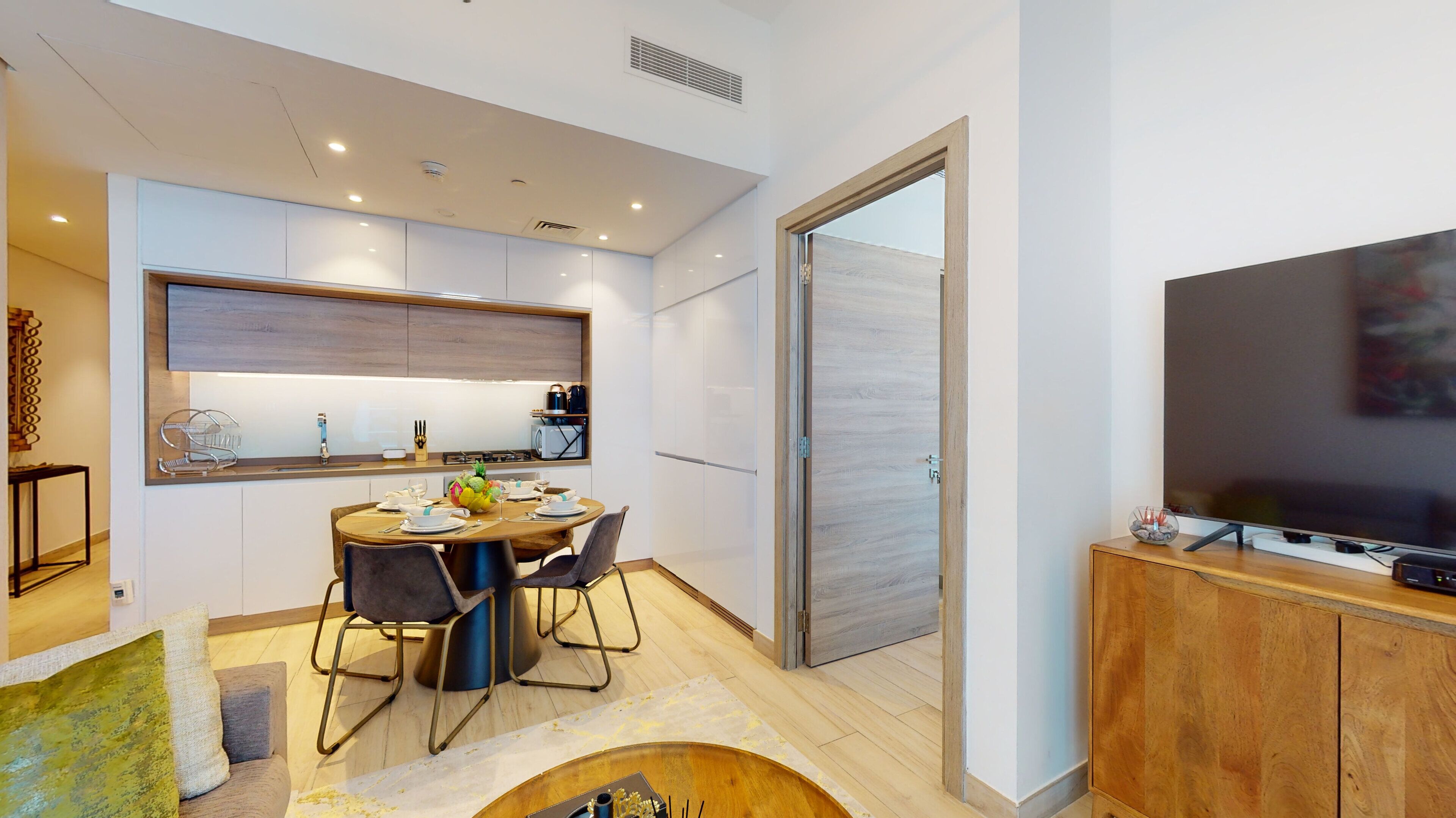 A modern kitchen with a dining area, a large flat-screen TV, and a sliding glass door leading to a balcony.