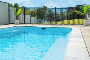 A rectangular swimming pool with a tiled edge, surrounded by a black metal fence, and potted plants on either side.