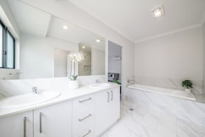 A modern bathroom with two sinks, a large mirror, and a bathtub.
