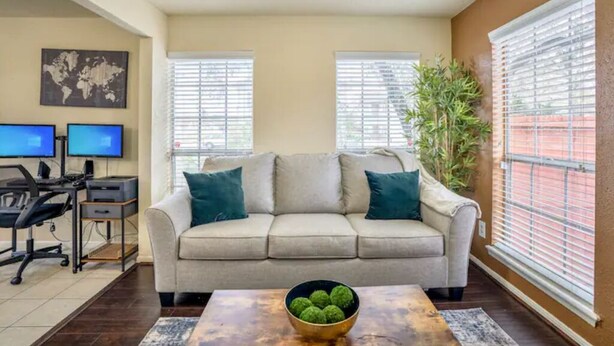 A living room with a beige sofa, two monitors on a desk, and a plant. - Entire Apt | Gated Parking | KING Bed | Computer (Houston)