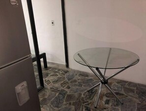 A small room with a glass-top table, a refrigerator, and a stone-patterned floor. - Comfortable, central and well located - Apt 202 (Medellín)