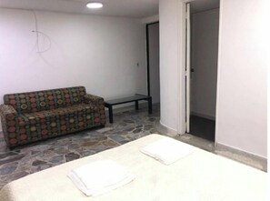 A room with a patterned sofa, a small table, and a bed with two folded white towels. - Comfortable, central and well located - Apt 202 (Medellín)