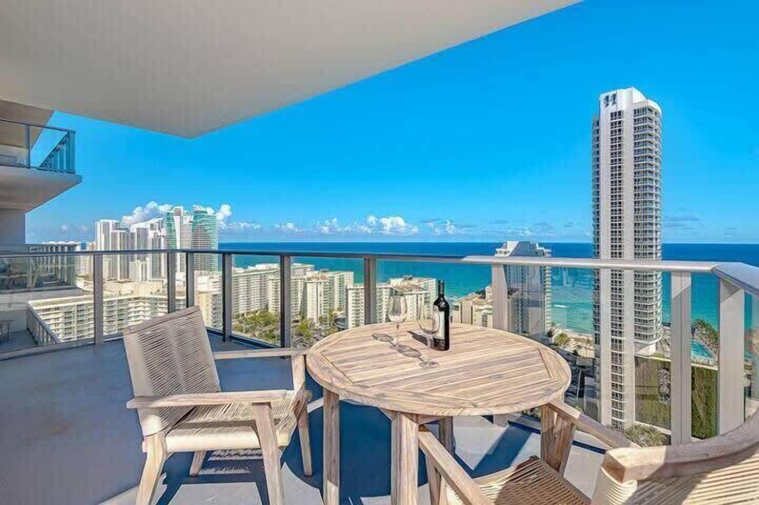 Een balkon met een ronde houten tafel, stoelen en een fles wijn.
