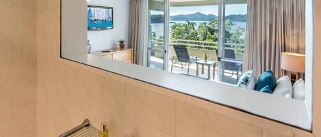 A hotel room with a large mirror reflecting a balcony with a view of the sea and mountains.