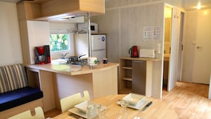 Una cocina compacta con microondas, estufa y cafetera. Hay un comedor con una mesa para dos personas, con platos, vasos y cubiertos.