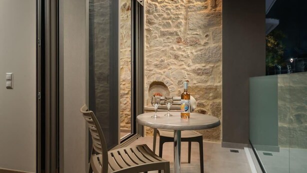 A balcony with a stone wall, a round table, two chairs, and a bottle of wine.
