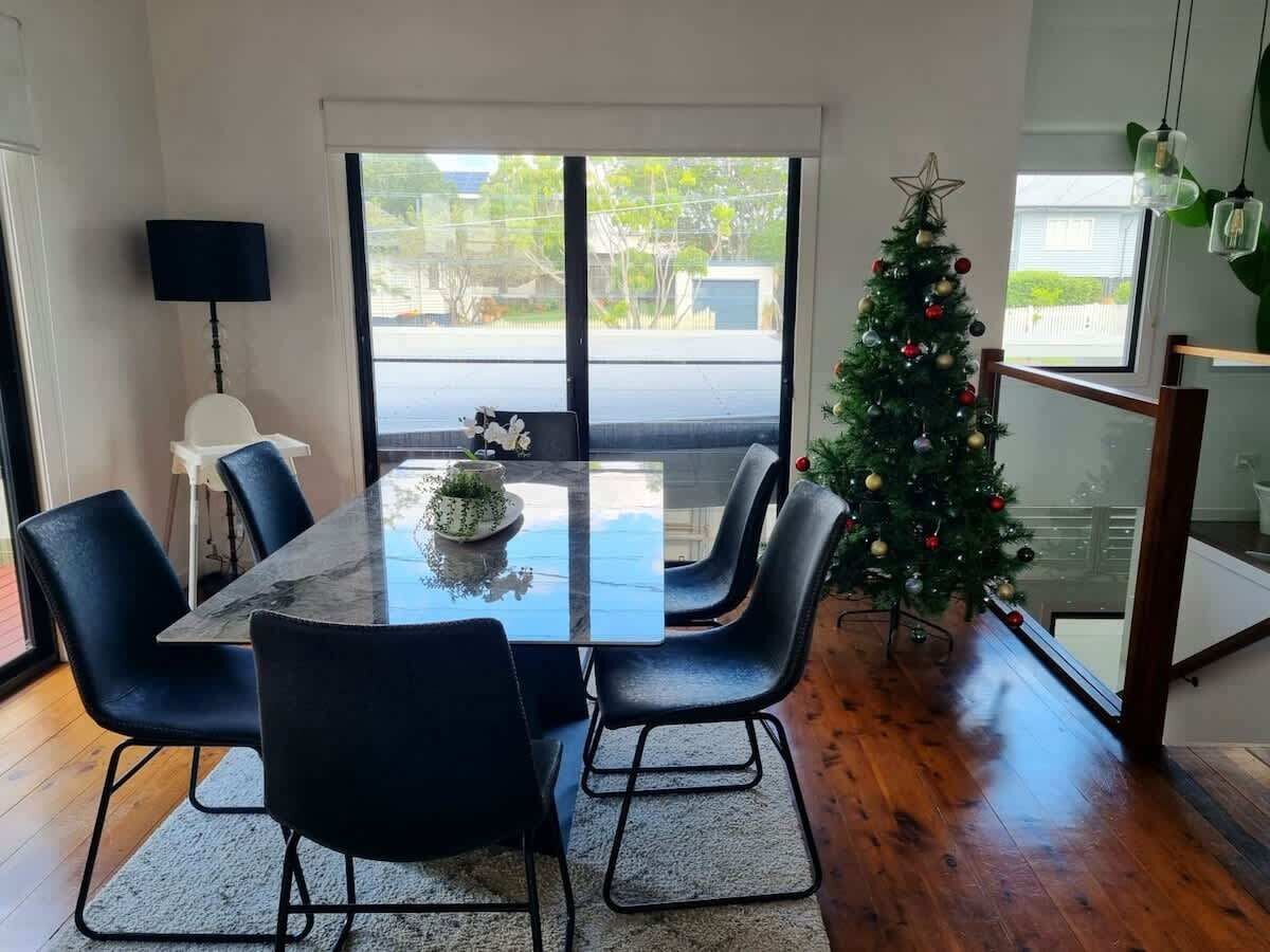 Una zona menjador moderna amb una taula de vidre, cadires negres, un arbre de Nadal i vistes a través de grans finestres.
