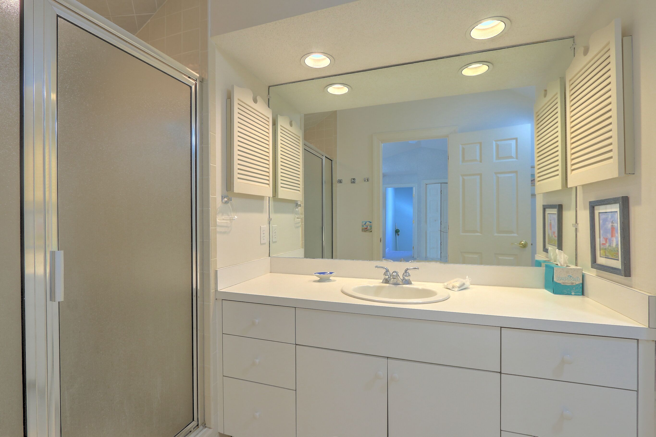 A bathroom with a large mirror, a sink, and a shower.