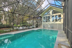 A swimming pool with a glass enclosure, surrounded by a deck with chairs and a staircase leading to a covered area with windows. - 21 Port Tack | 4 Bedroom Home | Enclosed Pool | Lagoon View | STR #065382 (Hilton Head Island)