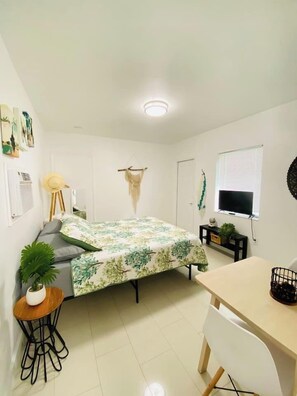 A small, well-lit room with a bed, a desk, a chair, a small table, and a television. - Authentic Little Havana • Walk to Calle Ocho (Miami)