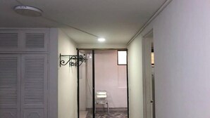 Un couloir étroit au sol carrelé, avec une porte blanche sur la gauche et une porte de placard à miroir sur la droite.