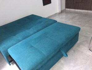 A teal sofa bed in a room with a tiled floor and a wooden door. - Comfortable, central and well located apartment - Apto 404 (Medellín)