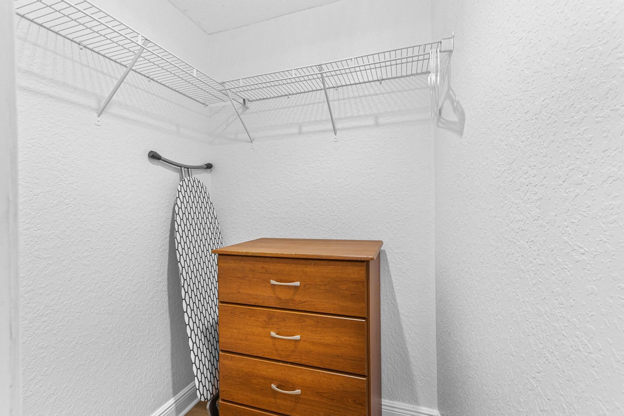 Un coin de pièce avec une commode en bois, une étagère en fil métallique et une serviette à motifs suspendue à un crochet.