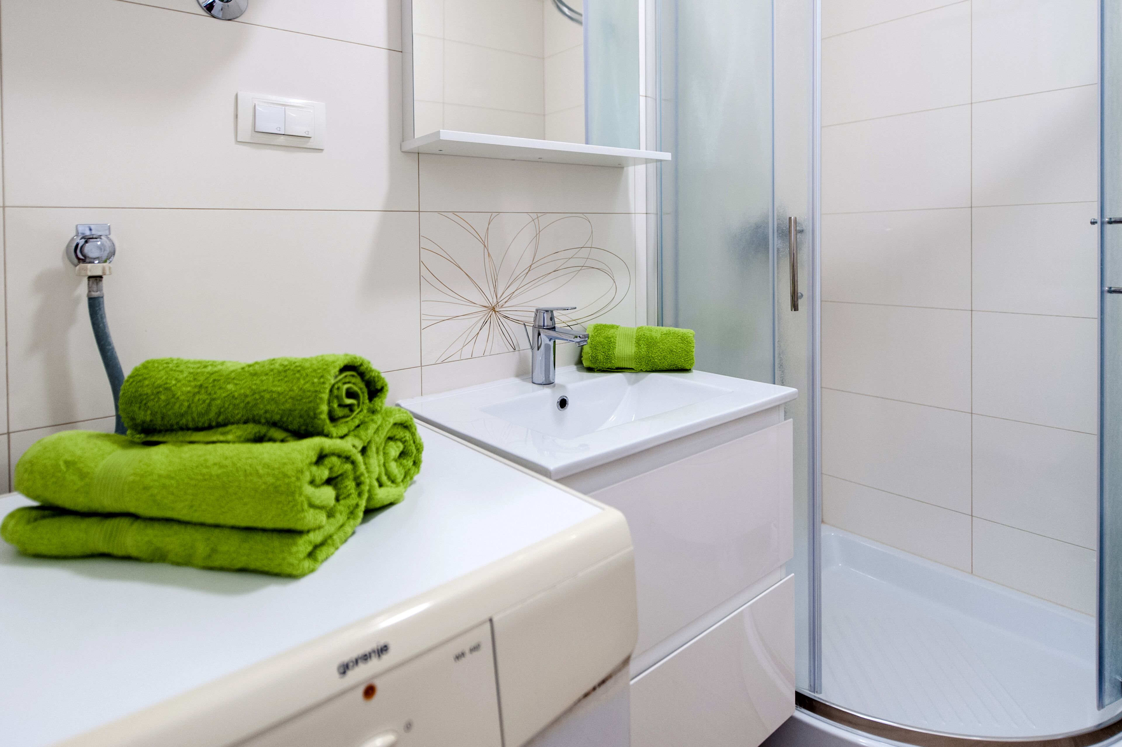 Une salle de bain avec un lavabo blanc, un miroir, une douche et une serviette verte posée sur le comptoir.